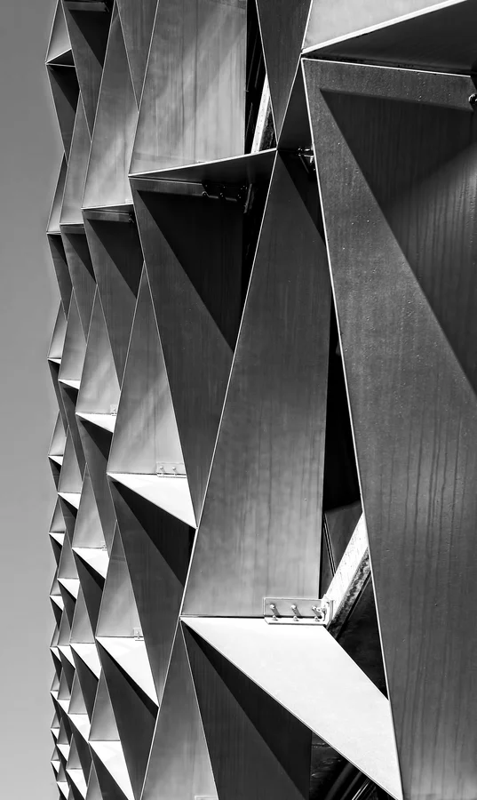 Fațadă arhitecturală cu panouri metalice triunghiulare pliate — tablă cu relief geometric, finisaj industrial