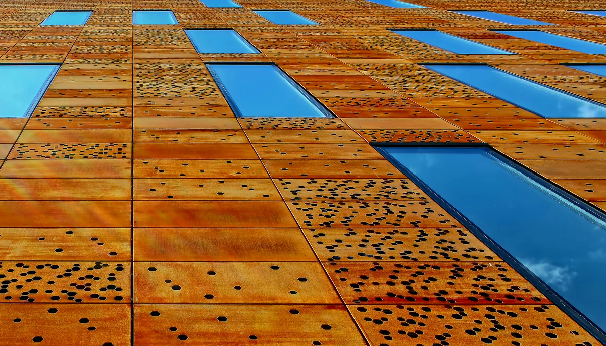 Fațadă arhitecturală din oțel Corten perforat cu decupaje circulare — panouri patinate natural, brun-portocaliu