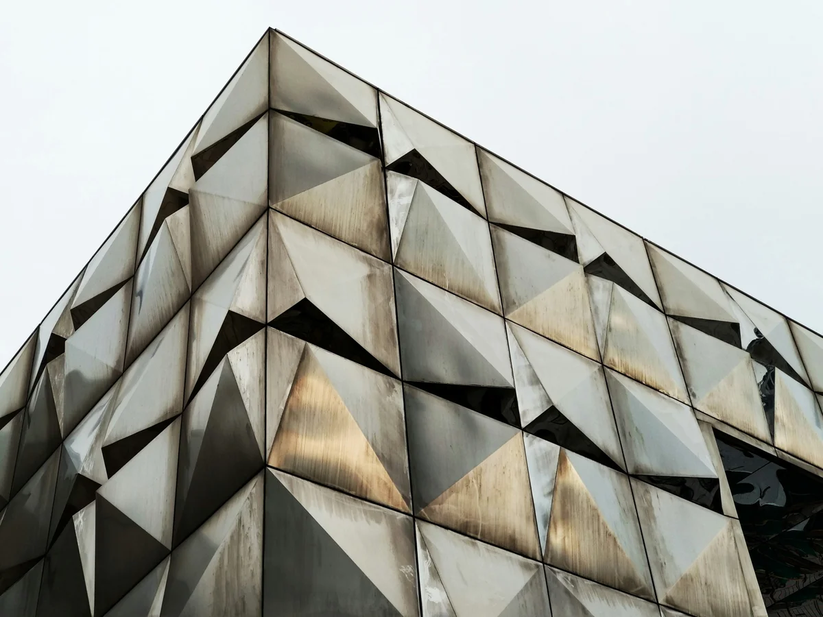 Fațadă arhitecturală cu panouri metalice geometrice triunghiulare — elemente decorative din tablă la comandă